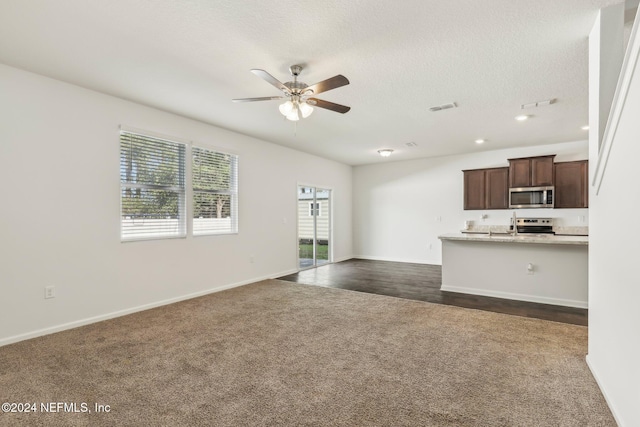 unfurnished living room featuring dark colored carpet, ceiling fan, and a textured ceiling