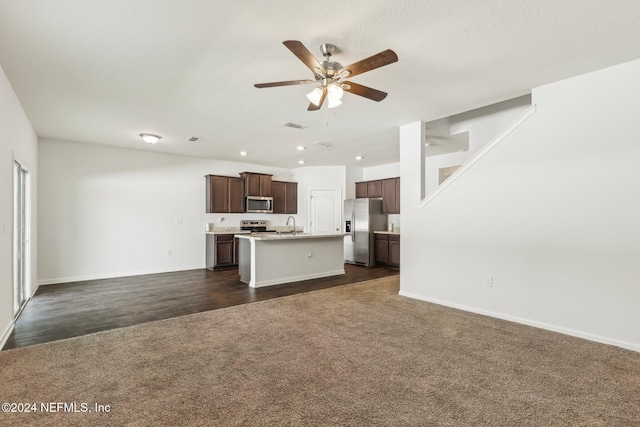 kitchen with dark wood-type flooring, a center island with sink, sink, ceiling fan, and stainless steel appliances