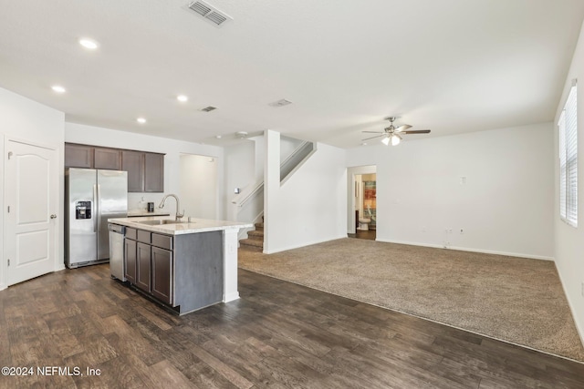 kitchen featuring dark carpet, a kitchen island with sink, sink, appliances with stainless steel finishes, and dark brown cabinetry