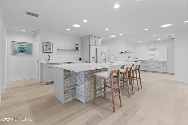 kitchen with high end white refrigerator, sink, a kitchen bar, a large island with sink, and light hardwood / wood-style floors