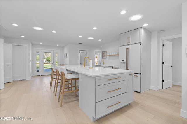 kitchen featuring high end fridge, light hardwood / wood-style flooring, a kitchen breakfast bar, and a center island with sink