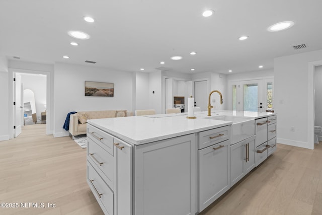 kitchen featuring a kitchen island with sink, sink, light hardwood / wood-style flooring, and gray cabinets