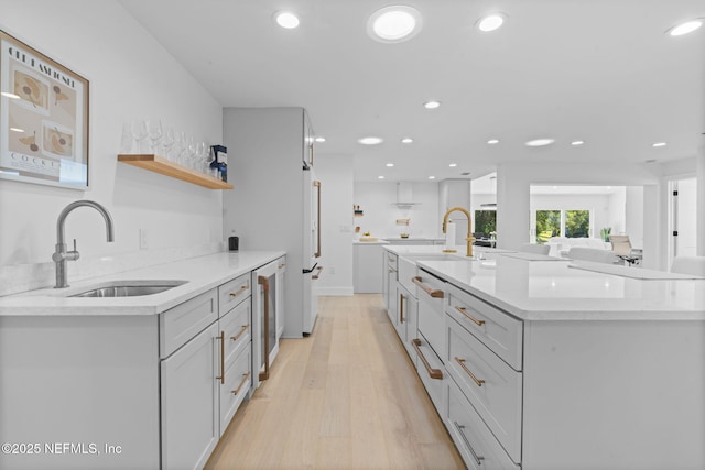 kitchen with light stone counters, sink, a center island with sink, and light wood-type flooring