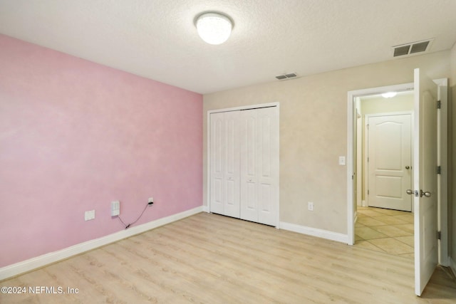 unfurnished bedroom featuring a textured ceiling, light hardwood / wood-style flooring, and a closet