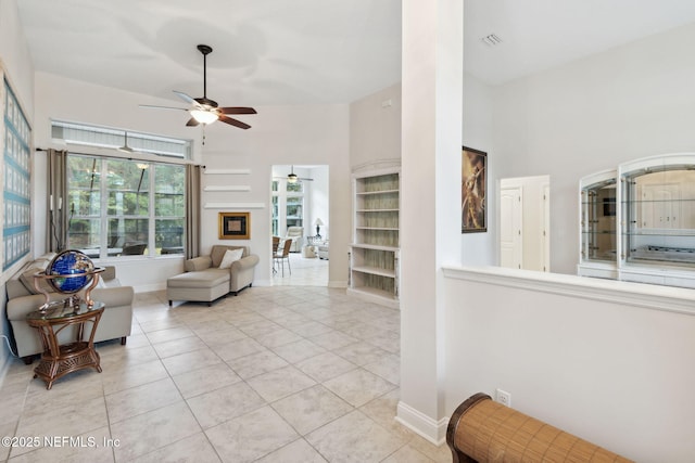 living room featuring built in shelves, light tile patterned floors, ceiling fan, and a high ceiling