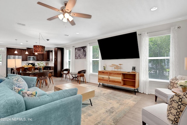 living room featuring ceiling fan, a healthy amount of sunlight, light wood-type flooring, and crown molding