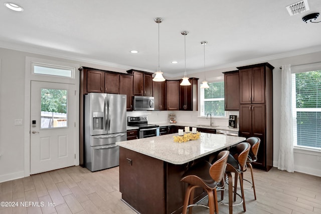 kitchen featuring a healthy amount of sunlight, a kitchen island, hanging light fixtures, and appliances with stainless steel finishes