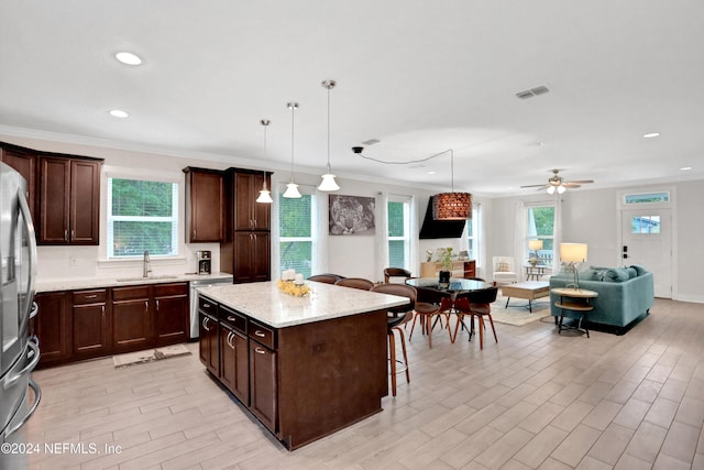 kitchen with pendant lighting, a breakfast bar, crown molding, ceiling fan, and a kitchen island