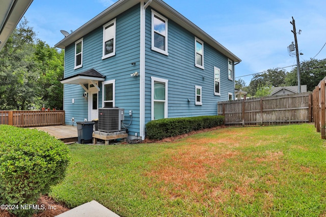 rear view of property featuring a lawn, a wooden deck, and central AC unit