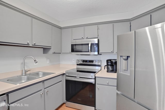 kitchen with stainless steel appliances, gray cabinetry, a textured ceiling, and sink