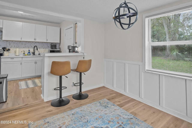 kitchen with sink, white cabinetry, hanging light fixtures, and light hardwood / wood-style flooring