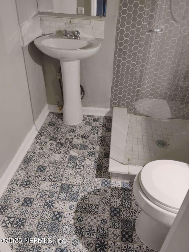 full bath featuring tile patterned flooring, toilet, baseboards, decorative backsplash, and a stall shower