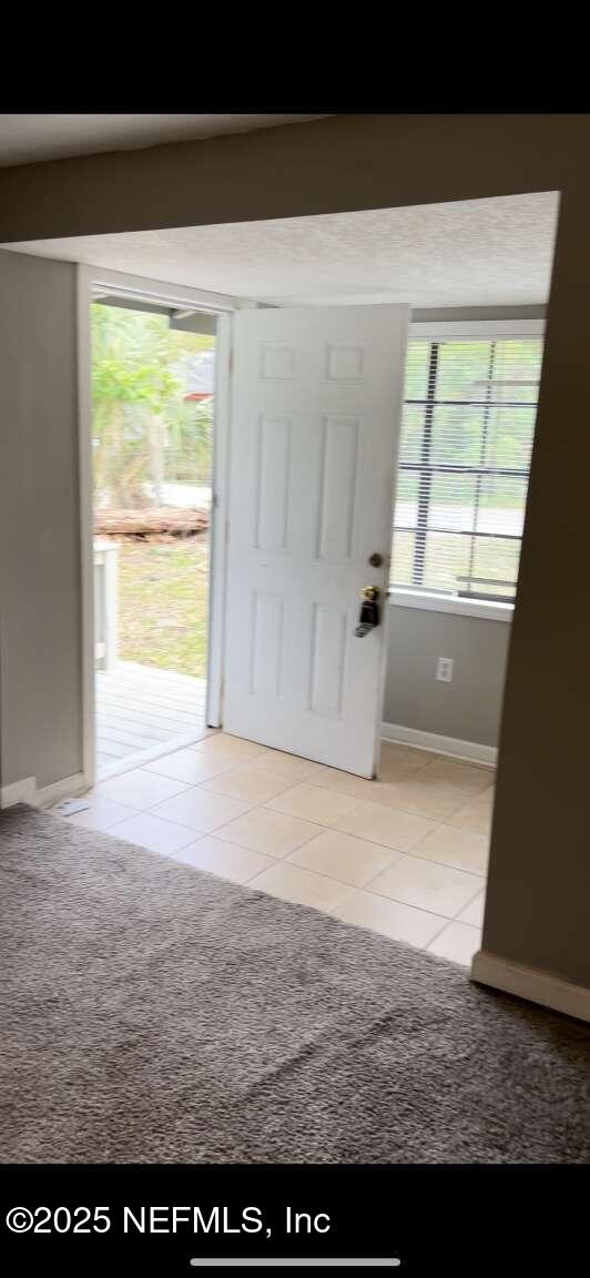 foyer entrance featuring light carpet, light tile patterned floors, plenty of natural light, and baseboards