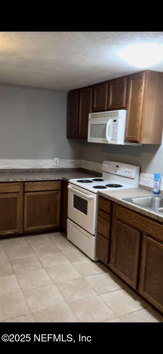 kitchen with white appliances, a textured ceiling, and a sink