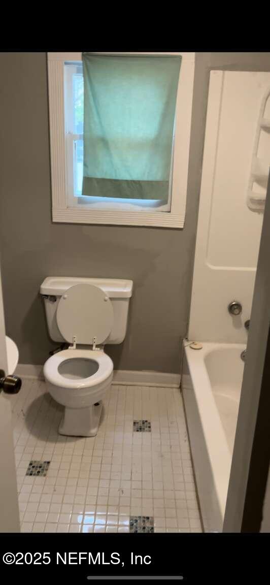 bathroom with toilet, tile patterned flooring, baseboards, and a bath