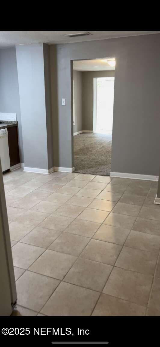 unfurnished room featuring light carpet, light tile patterned floors, and baseboards