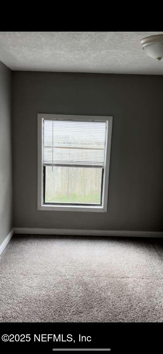 unfurnished room with a textured ceiling, carpet, and baseboards