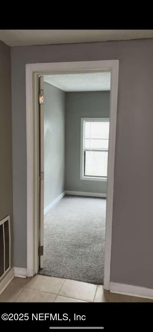 tiled empty room with carpet floors, visible vents, and baseboards