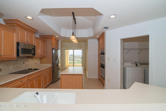 kitchen featuring a center island, a textured ceiling, a tray ceiling, washer and clothes dryer, and appliances with stainless steel finishes