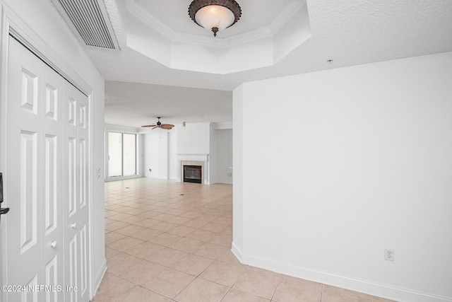 unfurnished living room with a tray ceiling, ceiling fan, light tile patterned flooring, and a textured ceiling