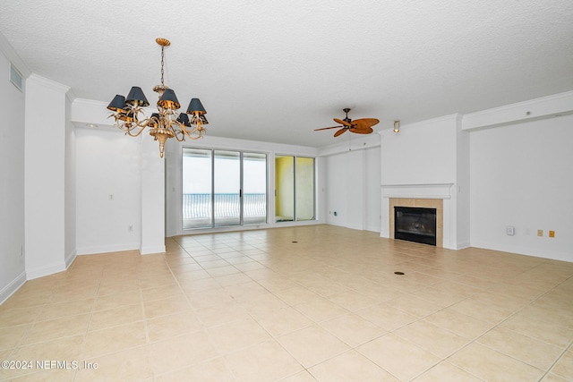 unfurnished living room featuring a textured ceiling, ceiling fan with notable chandelier, crown molding, a tiled fireplace, and light tile patterned flooring