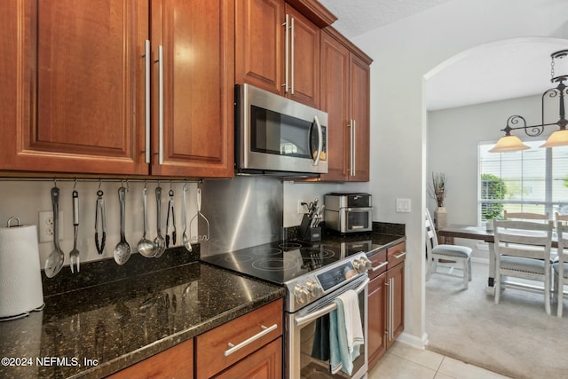 kitchen with a textured ceiling, dark stone countertops, light colored carpet, and stainless steel appliances