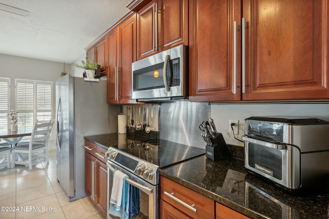 kitchen with light tile patterned floors, a textured ceiling, stainless steel appliances, and dark stone countertops