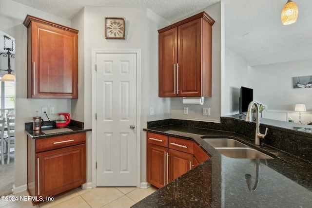 kitchen with light tile patterned floors, a textured ceiling, dark stone counters, and sink