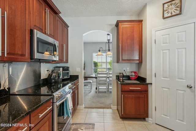 kitchen featuring dark stone countertops, light tile patterned flooring, stainless steel appliances, and a textured ceiling