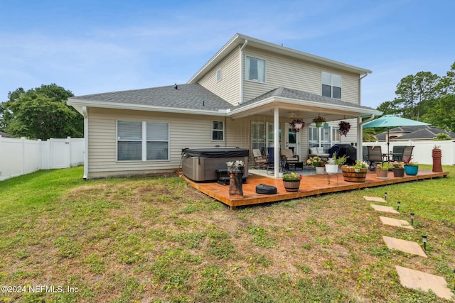 back of house featuring ceiling fan, a deck, a yard, and a hot tub