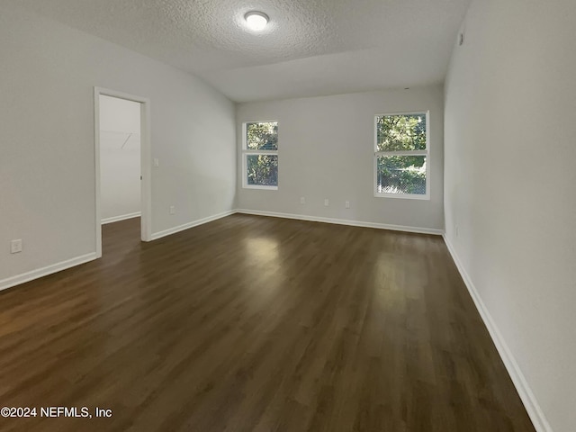 spare room with a textured ceiling, dark wood-type flooring, and lofted ceiling