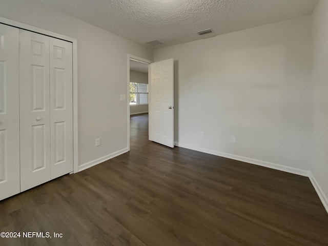 unfurnished bedroom with a textured ceiling, dark hardwood / wood-style floors, and a closet