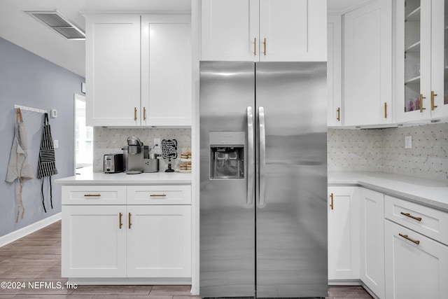 kitchen with light stone counters, stainless steel fridge, light hardwood / wood-style floors, decorative backsplash, and white cabinets