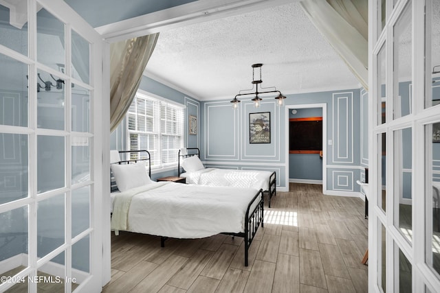 bedroom with a textured ceiling, hardwood / wood-style flooring, crown molding, and a notable chandelier