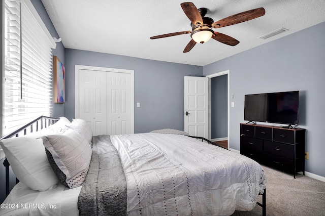 bedroom with ceiling fan, a closet, light carpet, and a textured ceiling