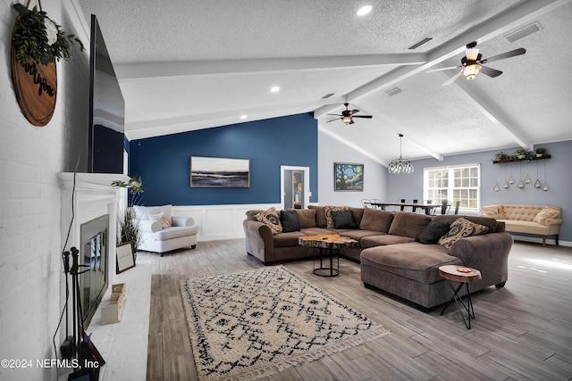 living room featuring vaulted ceiling with beams, light hardwood / wood-style flooring, ceiling fan with notable chandelier, and a textured ceiling