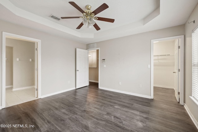 unfurnished bedroom featuring a raised ceiling, a walk in closet, dark hardwood / wood-style floors, and ceiling fan