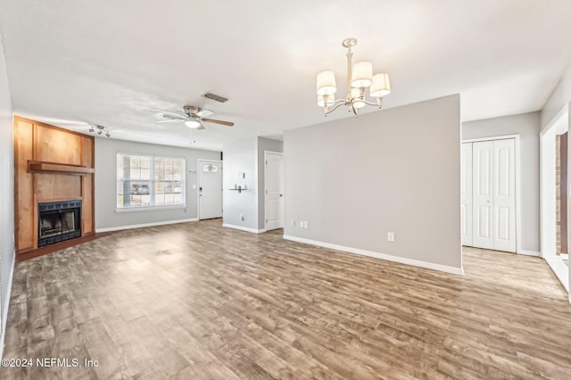 unfurnished living room with ceiling fan with notable chandelier, a fireplace, and hardwood / wood-style floors