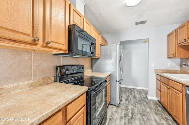 kitchen featuring sink, a textured ceiling, light hardwood / wood-style flooring, decorative backsplash, and black appliances