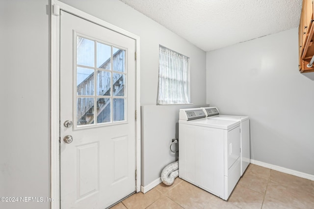 clothes washing area with light tile patterned flooring, washing machine and clothes dryer, a textured ceiling, and cabinets