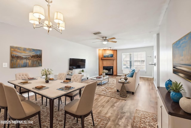 dining space with ceiling fan with notable chandelier, a tiled fireplace, and light hardwood / wood-style floors