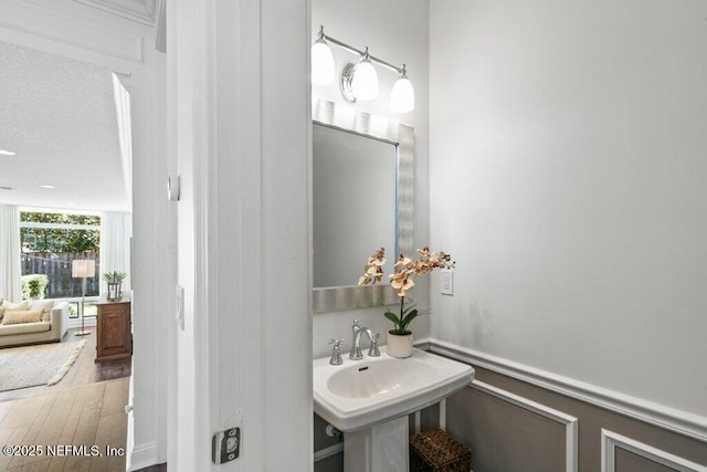 bathroom with a sink, a wainscoted wall, wood finished floors, and a textured ceiling