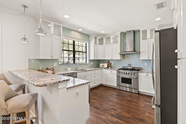 kitchen with appliances with stainless steel finishes, dark wood-type flooring, a sink, a peninsula, and wall chimney exhaust hood