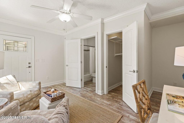 living area featuring baseboards, a ceiling fan, ornamental molding, a textured ceiling, and light wood-type flooring