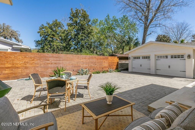 view of patio with outdoor dining space, an outdoor structure, fence, and a detached garage