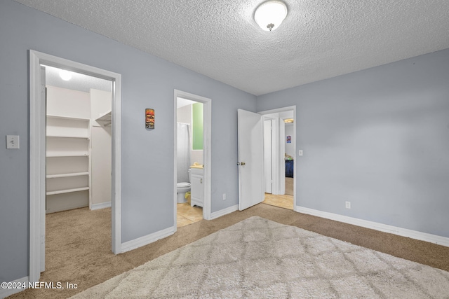 unfurnished bedroom with ensuite bath, a spacious closet, light colored carpet, a textured ceiling, and a closet