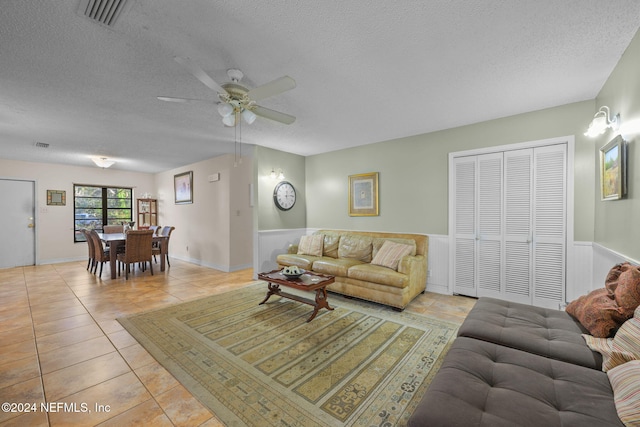 living room with ceiling fan, light tile patterned flooring, and a textured ceiling