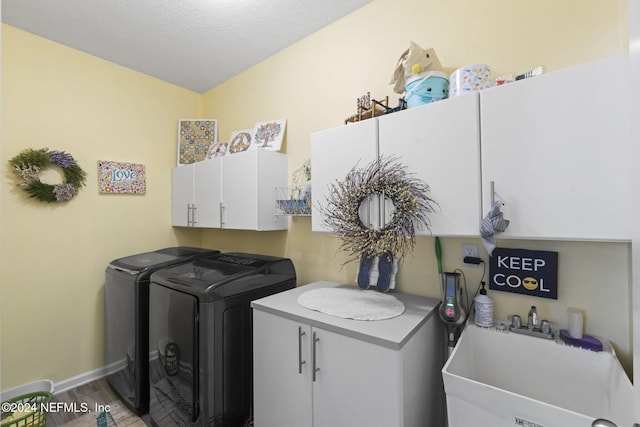 laundry room featuring hardwood / wood-style floors, a textured ceiling, washing machine and clothes dryer, sink, and cabinets