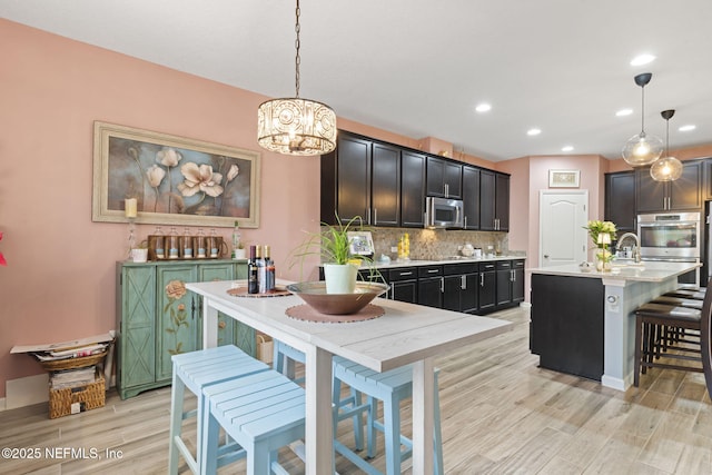 kitchen with stainless steel appliances, hanging light fixtures, a center island with sink, and tasteful backsplash