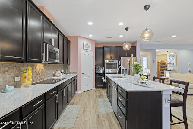 kitchen featuring appliances with stainless steel finishes, an island with sink, a kitchen breakfast bar, backsplash, and hanging light fixtures